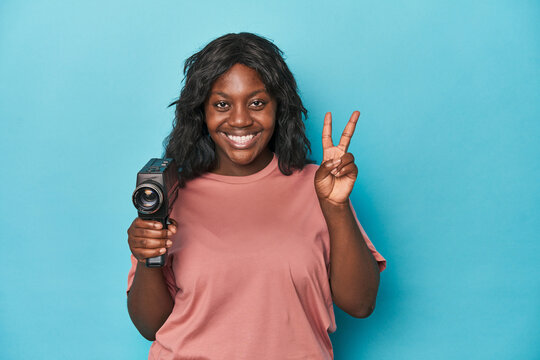 Curvy lady with vintage film camera showing number two with fingers. - Powered by Adobe