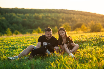 Сouple is playing with a kind black domestic dog in the forest, on a  summer day.Beautiful sunny landscapes around them.Family playing with dog
