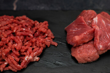 Close-up side view of chunks of beef meat and minced meat lying on a black cutting board on the...