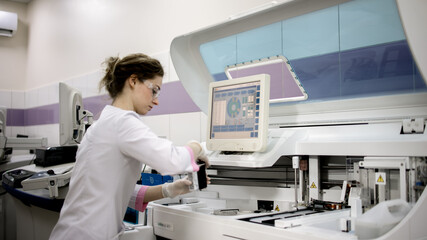 A young woman works in a modern laboratory with advanced equipment and an analyzer. The concept innovative technologies and top-notch equipment for precise scientific research.