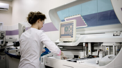 A young woman works in a modern laboratory with advanced equipment and an analyzer. The concept...