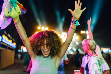 Enthusiastic young woman dancing with rainbow scarf at night music festival