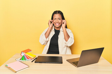 Indonesian designer with tools at table on yellow showing fist to camera, aggressive facial...