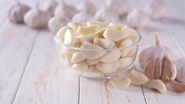 peeled garlic cloves in a transparent bowl on a white wooden table.