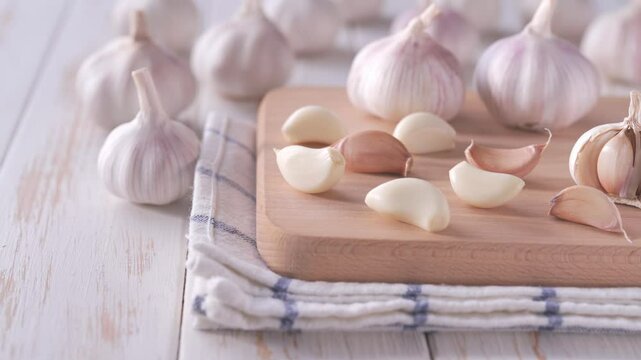Organic garlic cloves and bulbs on a cutting board, in background a pile of garlic unpeeled.