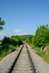 Obraz premium Railway track surrounded by green nature under a blue sky