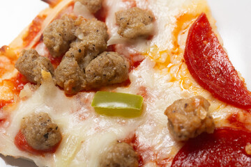 Slice of fresh Italian classic original sausage and pepperoni supreme pizza with green pepper and cheese on a white glossy plate