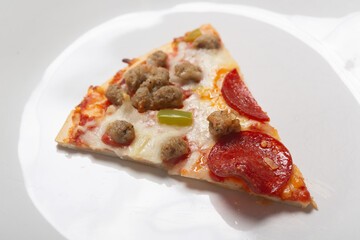 Slice of fresh Italian classic original sausage and pepperoni supreme pizza with green pepper and cheese on a white glossy plate