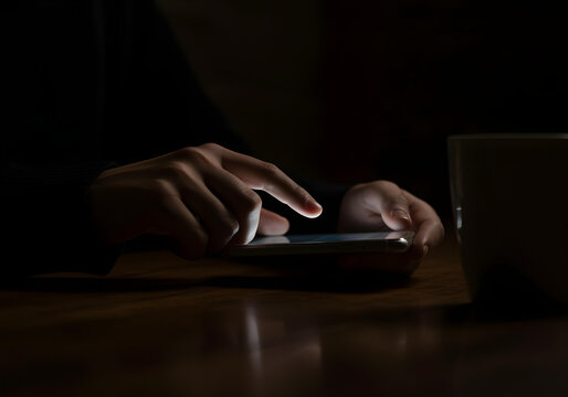 A close-up of hands interacting with a smartphone on a wooden surface in low-light conditions.