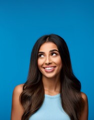 Naklejka premium Close-up portrait of a cheerful young woman with long hair, looking curiously at copy space on a vibrant blue background. 