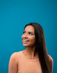 Fototapeta premium Close-up portrait of a cheerful young woman with long hair, looking curiously at copy space on a vibrant blue background. 