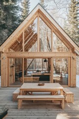 Modern wooden cabin in the forest features large glass windows, a spacious deck, and a cozy dining area surrounded by trees and snow in a serene winter setting