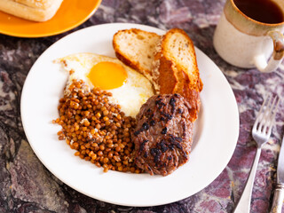 Appetizing roasted beef hamburger cutlet served with lentils and fried egg on platter