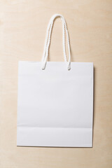 Recyclable white paper shopping bag on a birch wood panel background with a white fabric braided handle. can be used for a mockup for design