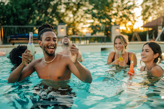 Friends enjoying drinks and laughing in swimming pool at sunset party