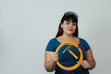 Smiling woman holding a yellow cable and hammer, ready for work. Wearing a blue shirt and safety goggles, she represents confidence and skill. Ideal for construction, DIY, and repair themes.