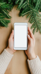 A hand gently holds a smartphone with a blank screen while resting on a wooden surface. The surrounding pine branches add a touch of nature creating a cozy and inviting atmosphere
