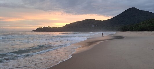 Um turista passeando durante o pôr-do-sol em um dia nublado com muitas cores no céu, na praia do Félix, em Ubatuba, litoral norte paulista, Brasil. © Ricardo_S_Levenhagen