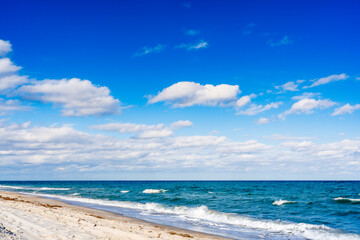 Obraz premium waves crashing on beach with clouds in blue sky