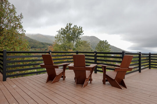 Adirondack chairs on a wooden deck facing a beautiful mountain range covered in morning haze