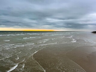 Wide expanse of beach with shallow tide beneath moody sky and setting sun
