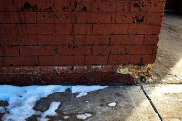 close-up of rustic crumbling corner of red brick exterior wall with spalling and snow on pavement...
