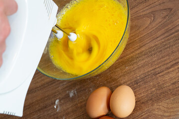 Mixing whisking raw yellow eggs with white mixer. Cooking omelette, pancakes blini with family....
