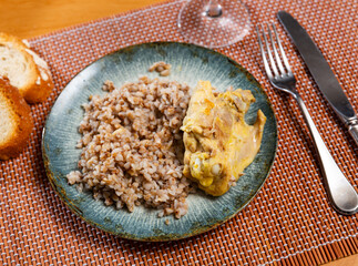 Prepared buckwheat porridge with piece of fried chicken is served on large white platter with bread. High quality photo