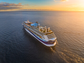 Cruise ship sailing across tranquil ocean waters at sunset with a vibrant sky and reflective surface