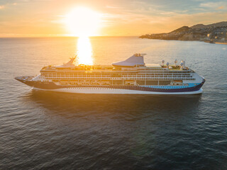 Luxury cruise ship sails towards Funchal, Madeira, during a vibrant sunset on the ocean horizon for...