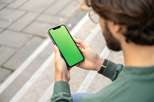 Young man holding smartphone while sitting on outdoor steps in a city environment during the daytime
