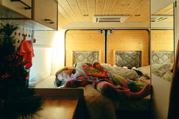 Caucasian female child relaxing in cozy camper bed with book and christmas decorations