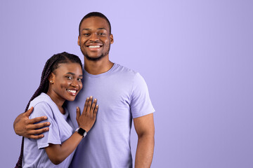 Obraz premium Love, Care And Tenderness. Portrait of smiling African American woman and man hugging, enjoying time together, standing isolated over purple studio background, posing and looking at camera