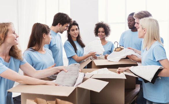 Young volunteers group sorting clothing donations in cardboard boxes, copy space