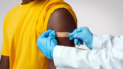 Doctor Applying Plaster On Arm Of Black Male Patient After Vaccine Shot, Closeup Shot Of...