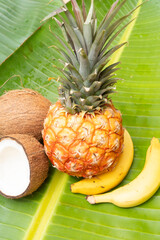 A vibrant and juicy pineapple sitting alongside a beautiful yellow flower, both resting on lush green tropical leaves