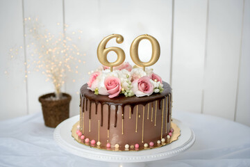 60th birthday chocolate cake with a gold topper, floral decoration rich frosting and a glaze placed on a white table