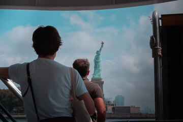 Distant view of the Statue of Liberty on Liberty Island, New York City, with a cloudy sky, with two people in the foreground.