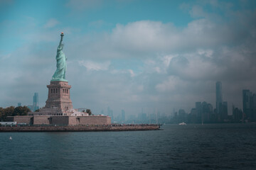Distant view of the Statue of Liberty on Liberty Island, New York City, with a cloudy sky.