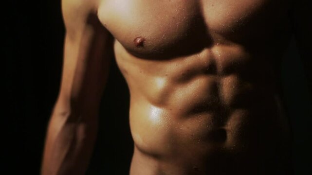 Muscular nude man flexing his body. Sexy male torso closeup. Shirtless man showing abs and muscles. Athletic male body in dramatic lighting. Sexy muscular man posing nude. Man flexing muscles.