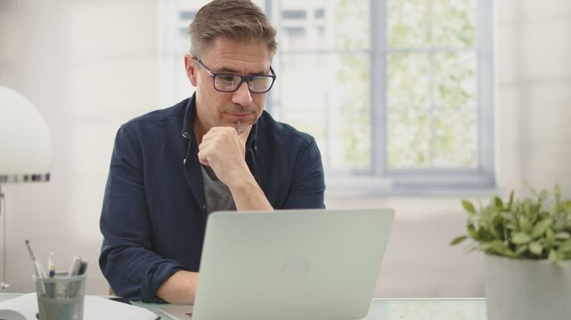 Businessman working in office with computer sitting at desk. Portrait of mature age, middle age, mid adult man in 40s.