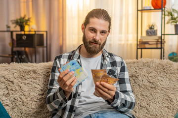Young man inspects fresh money cash banknotes at home, carefully sorting each euro with measured...