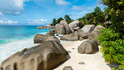 Turquoise waters washing over a white sandy beach with rocks. Seychelles, Mahe. Carana beach.