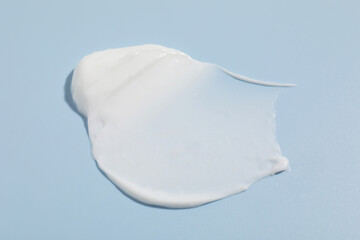 Sample of cream on light blue background, closeup. Cosmetic product