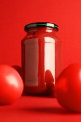 Ketchup in glass jar and fresh tomatoes on red background