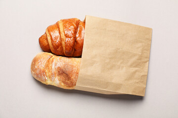 Paper bag with fresh baguette and croissant on light gray table, top view