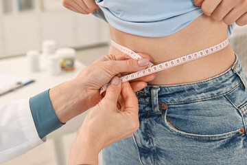Weight loss. Nutritionist measuring patient's waist with tape in clinic, closeup