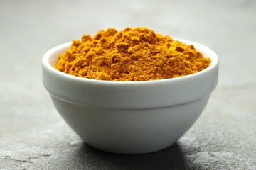 Turmeric powder in bowl on grey table, closeup