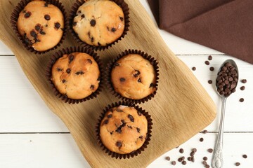 Delicious muffin with chocolate chips on white wooden table, flat lay