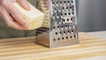 chef grating traditional parmesan cheese with steel grater on the wooden board
